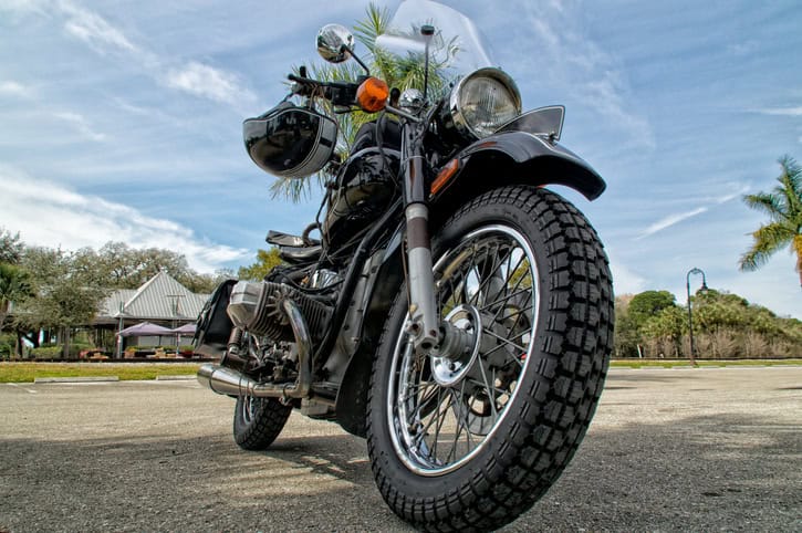 Low angle view black vintage motorcycle the knobby tires and matching helmet hanging from handlebars in tropical florida setting.